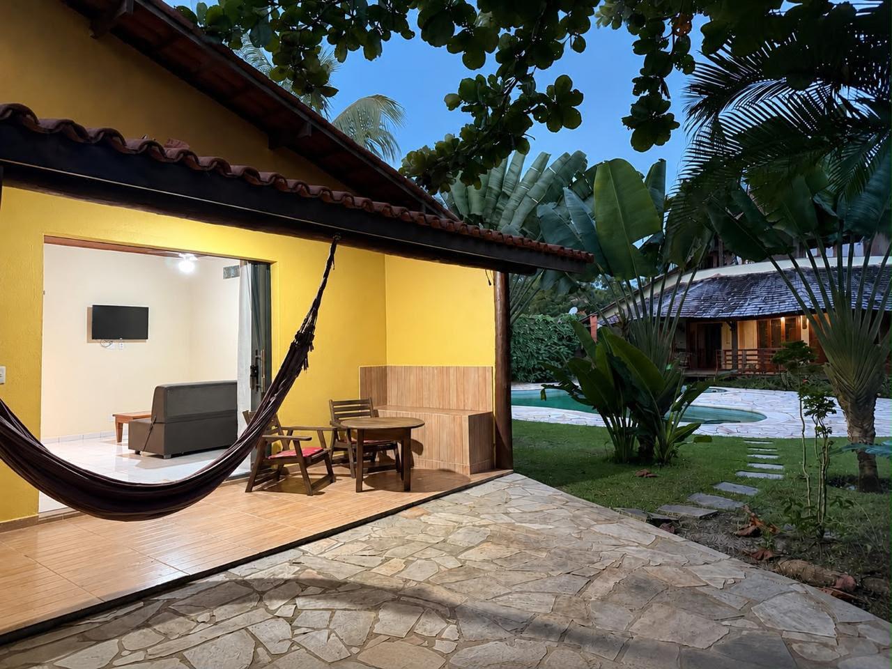 Chalé com varanda e rede, com a casa ao fundo
